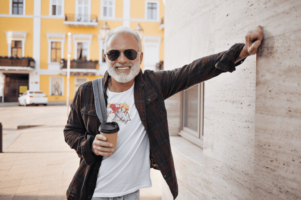 man in sunglasses holding cup of coffee and wearing white unisex tshirt with artistic poster print of two cartoonish figures racing bicycles white unisex tshirt with artistic poster print of two cartoonish figures racing bicycles