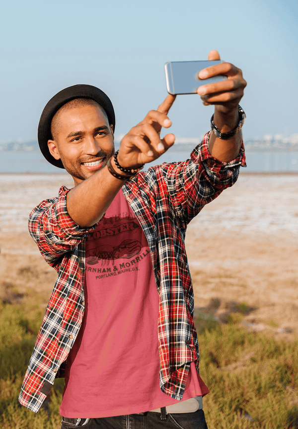 man in a hat taking a selfie and wearing heather red mens tshirt with vintage graphic logo of lobster brand